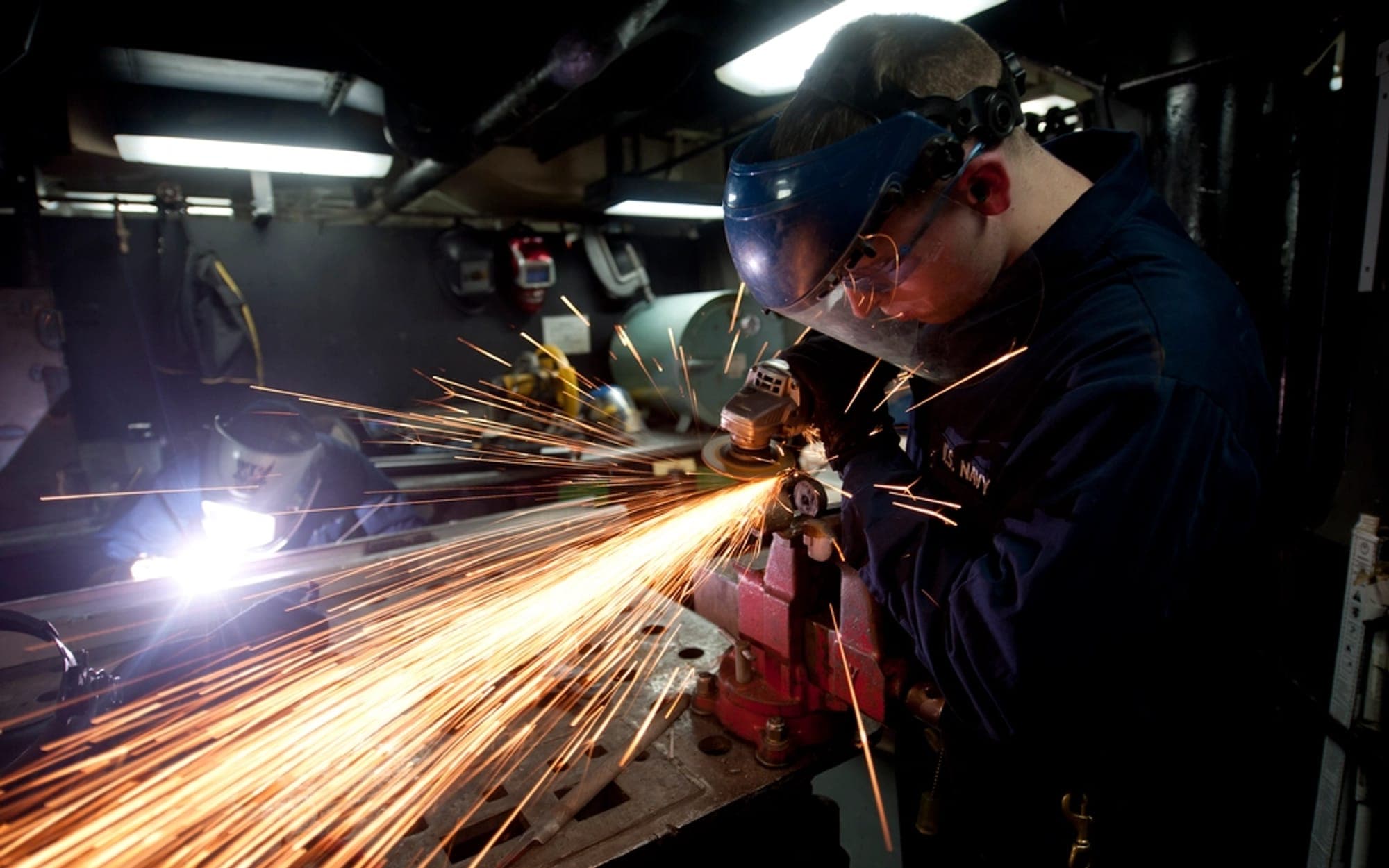 Worker in a welding mask grinding metal, throwing sparks