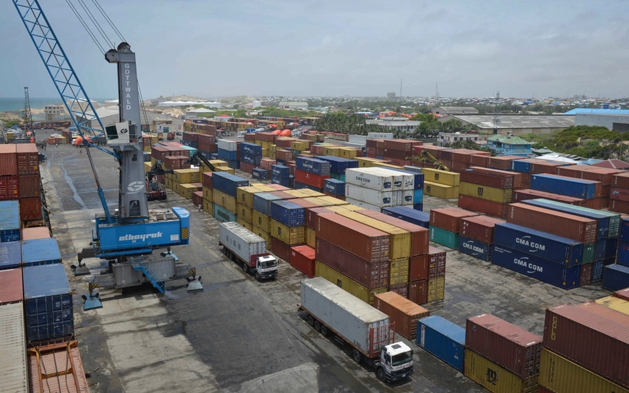 Container yard with a crane and lorries between stacked containers