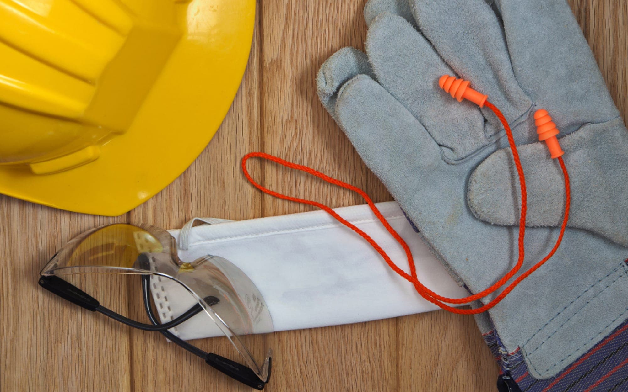 Hard hat, safety glasses, gloves, ear protection and a mask laid on a bench