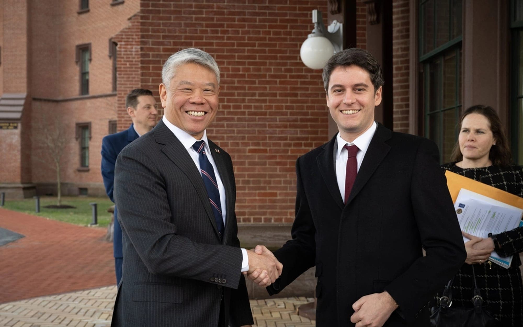 Two people shaking hands outdoors while colleagues look on