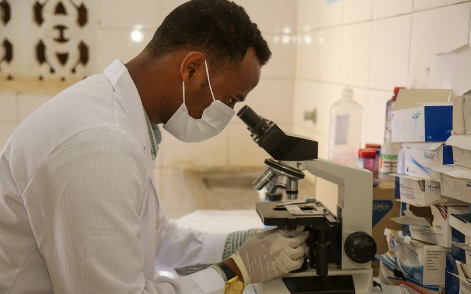 Technician in a laboratory coat and mask working at a microscope